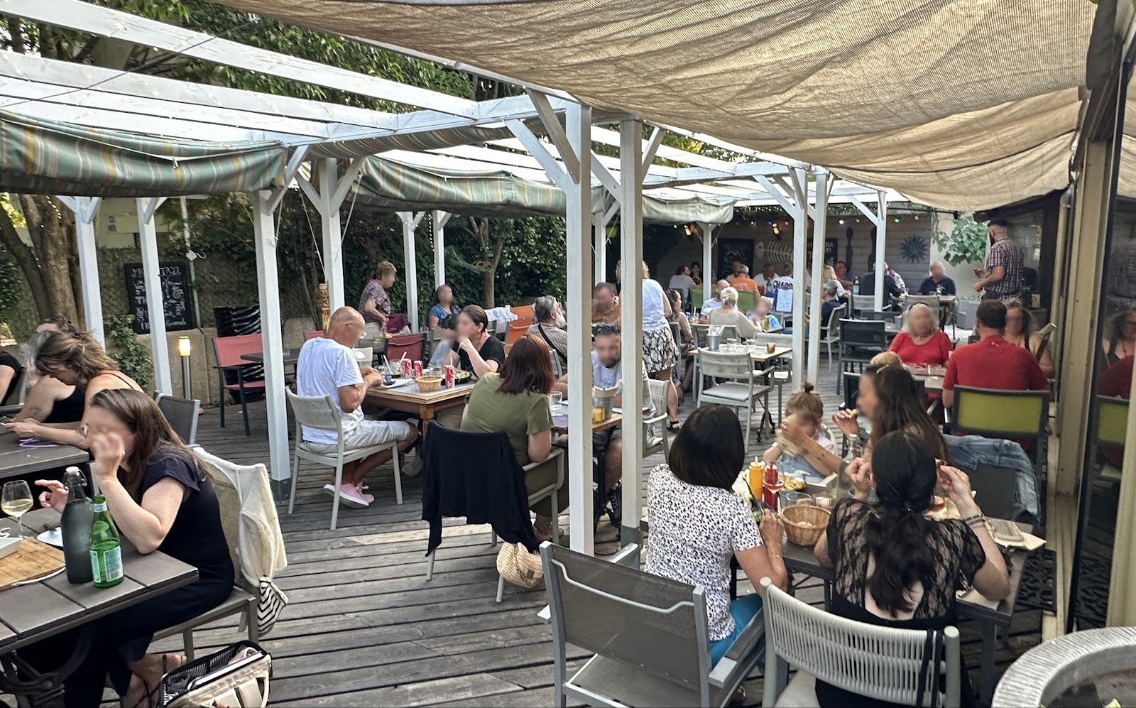 Terrasse animée d'un restaurant en plein air sous pergola avec voiles d'ombrage