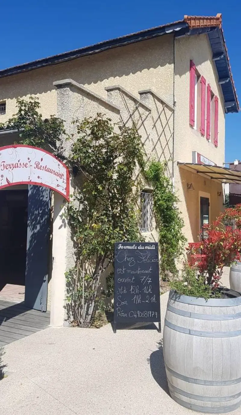 Façade ensoleillée du restaurant Chez Félicien avec terrasse et tonneau décoratif