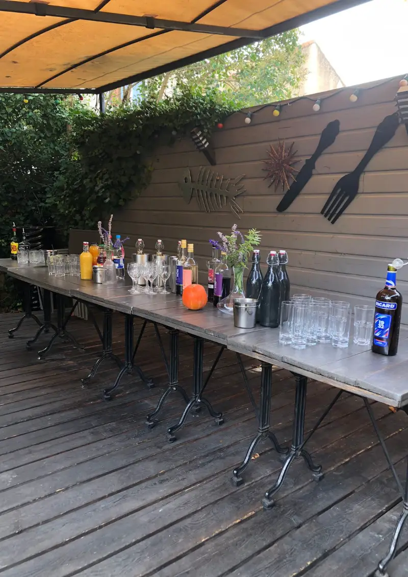 Terrasse extérieure avec tables et bar dressé sous pergola, bouteilles et verres